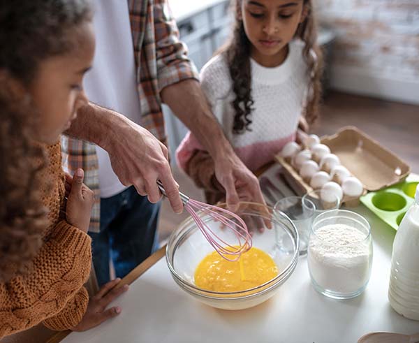 Girls watching their father whipping eggs while cooking pie
